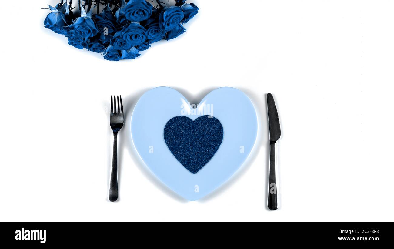 Classico colore blu di impostazione per San Valentino con belle rose, forchetta, coltello e piatto a forma di cuore su sfondo bianco. Alla moda colo Foto Stock