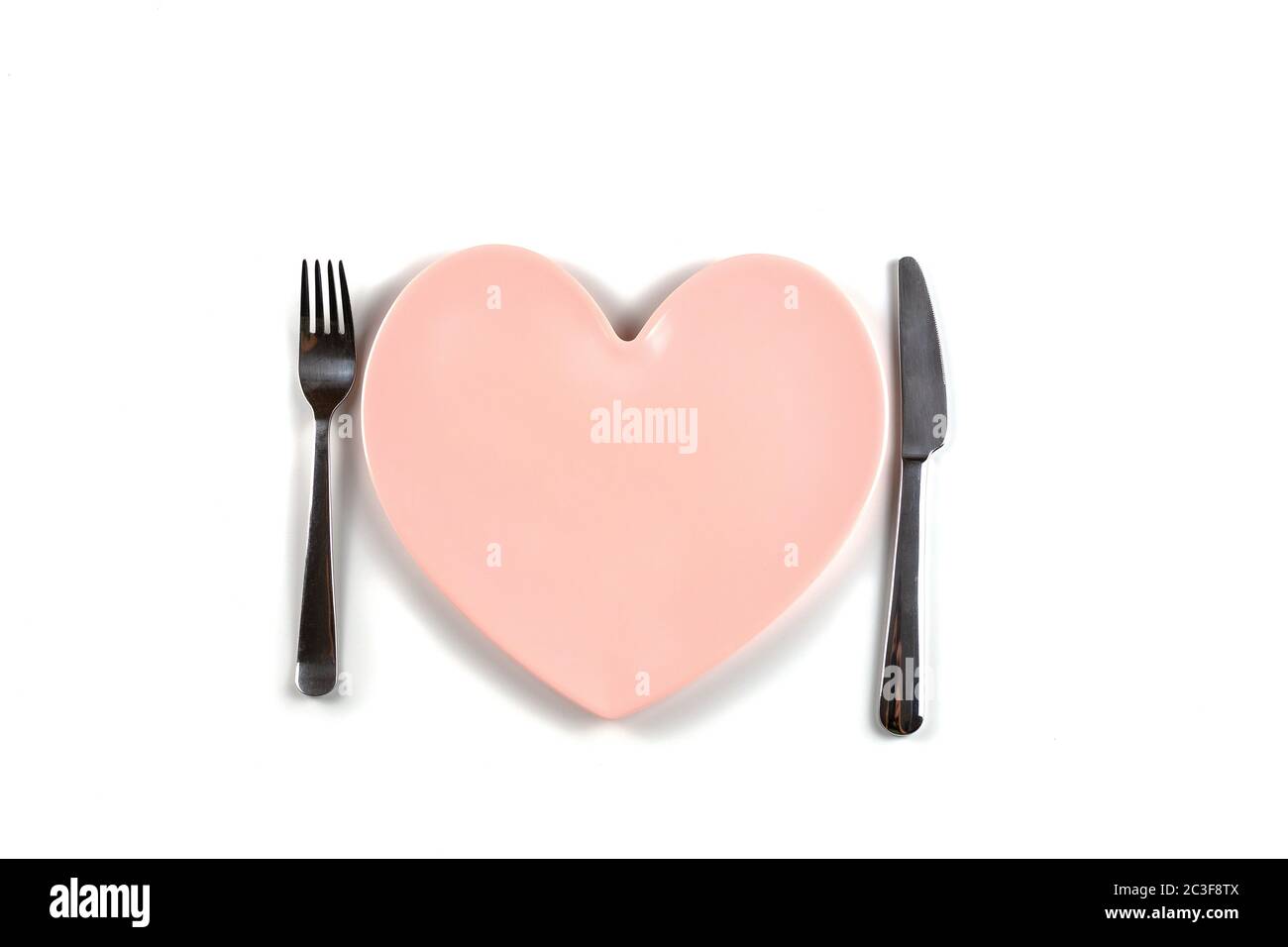 Piastra rosa vuota a forma di cuore, coltello da tavolo e forchetta su sfondo bianco. Minimalismo. Spazio di copia. Piatti moderni in ceramica lucida. Concetto di Foto Stock