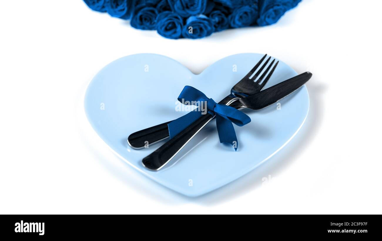 Classico colore blu di impostazione per San Valentino con belle rose, forchetta, coltello e piatto a forma di cuore su sfondo bianco. Alla moda colo Foto Stock