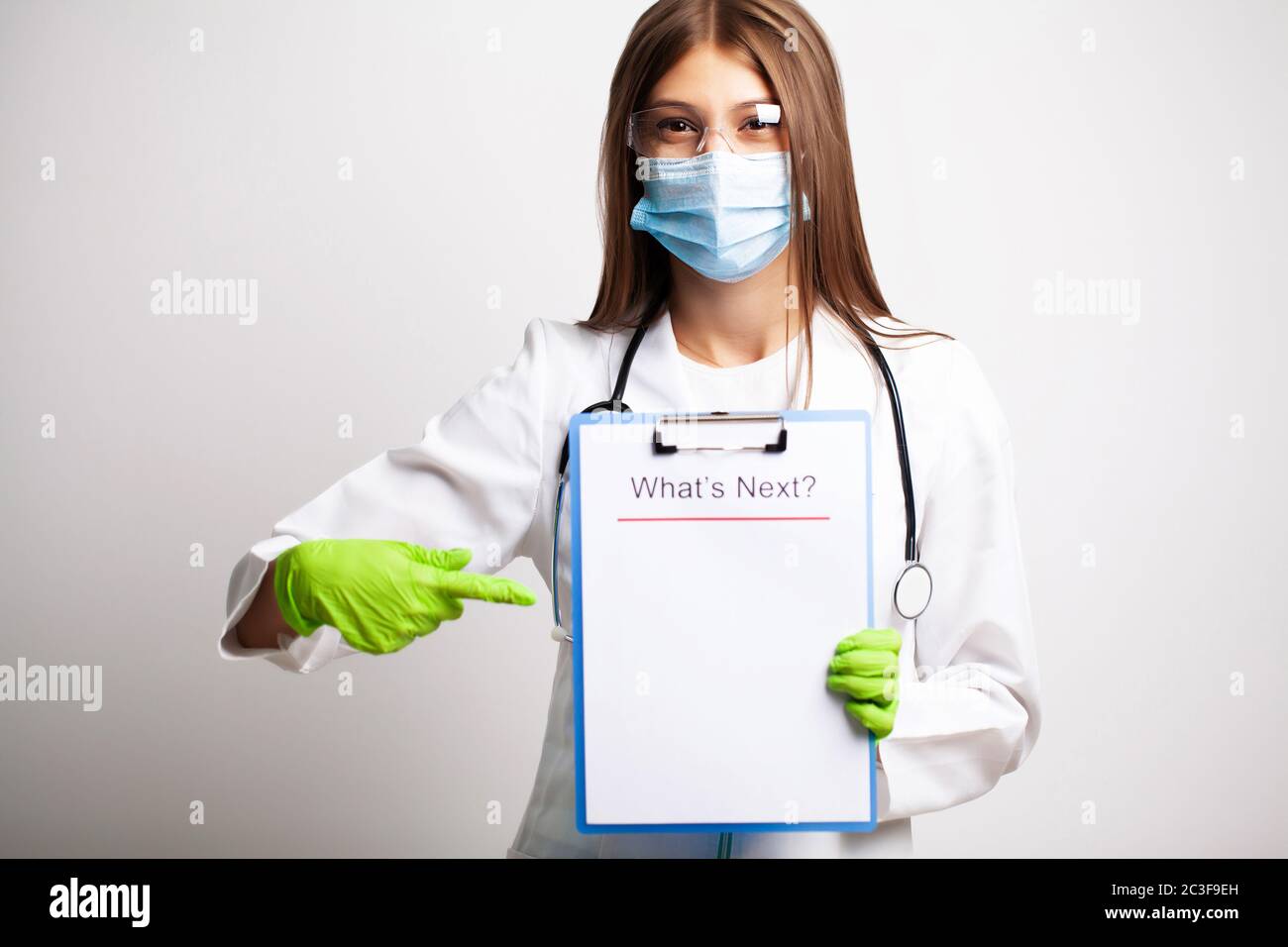 Giovane dottore in una maschera guarda la macchina fotografica e tiene un foglio di carta con il testo che cosa è prossimo Foto Stock