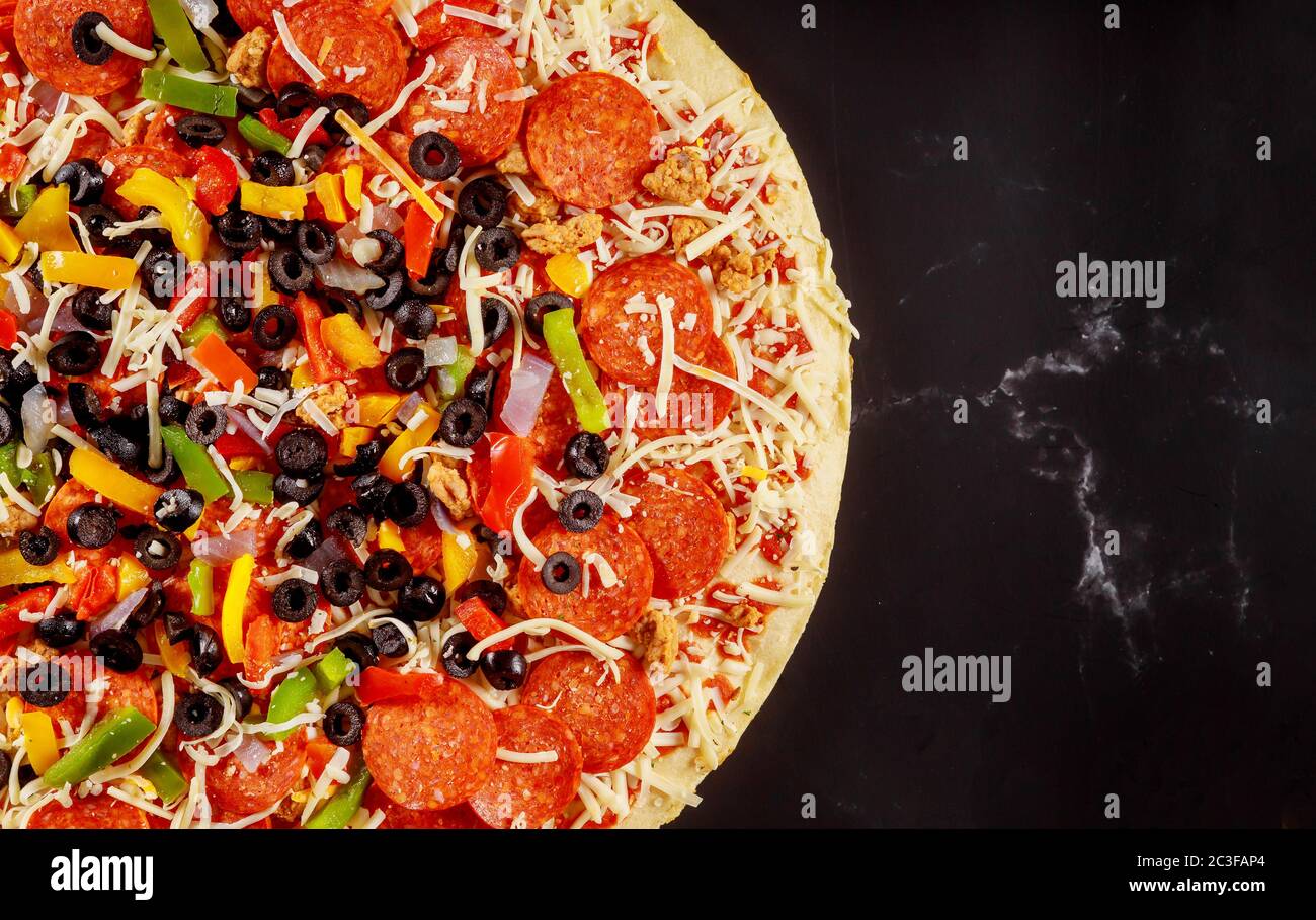 Pizza suprema con pomodoro, salame, olive con crosta spessa su tavola nera. Foto Stock