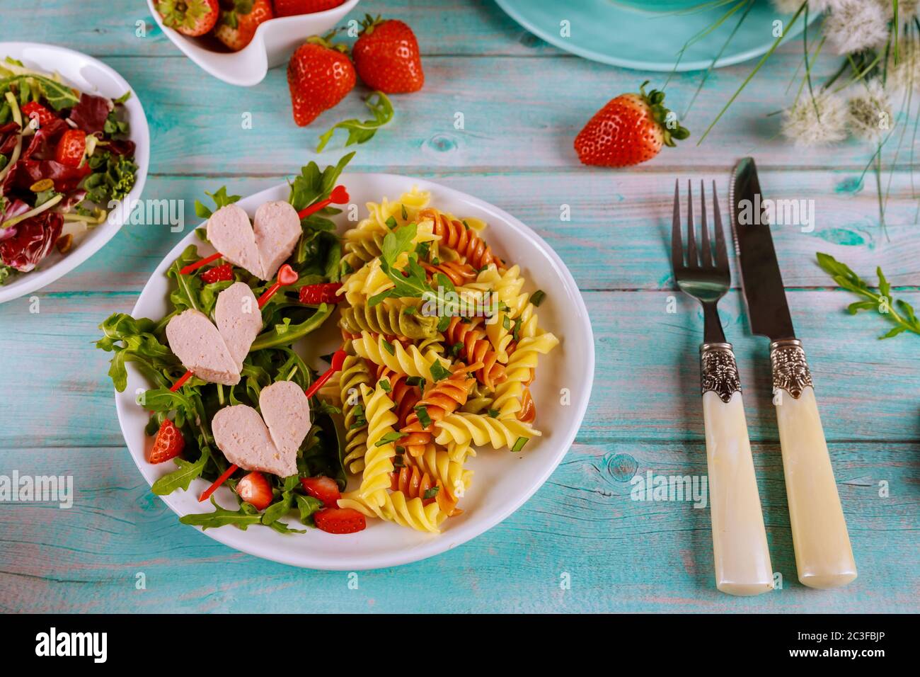 Gustosa pasta rotini di colore con salsicce, fragola fresca su sfondo blu di legno. San Valentino, cena per coppia. Foto Stock