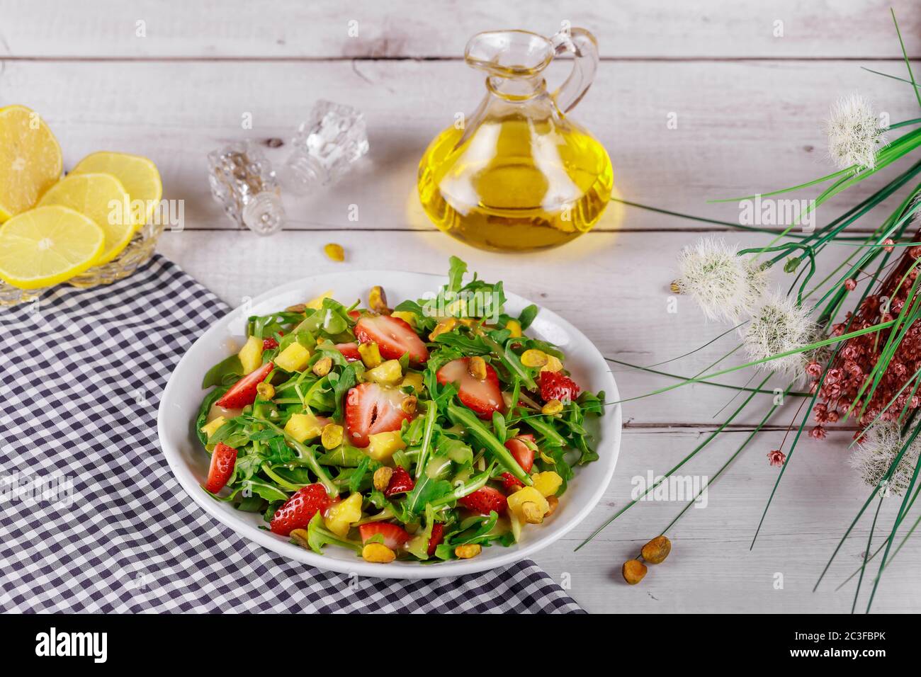 Insalata di fragole con rucola, mango e pistacchi con limone e olio d'oliva su tavola di legno con fiori. Foto Stock
