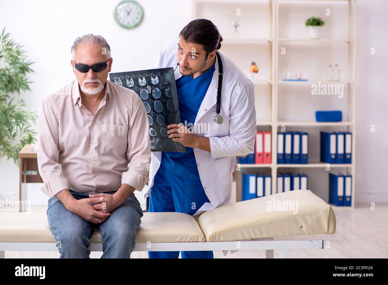 Vecchio cieco che visita il medico giovane maschile Foto Stock