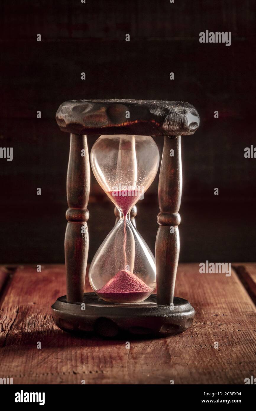Il tempo sta esaurendo il concetto. Una clessidra con sabbia che cade su uno sfondo rustico scuro Foto Stock