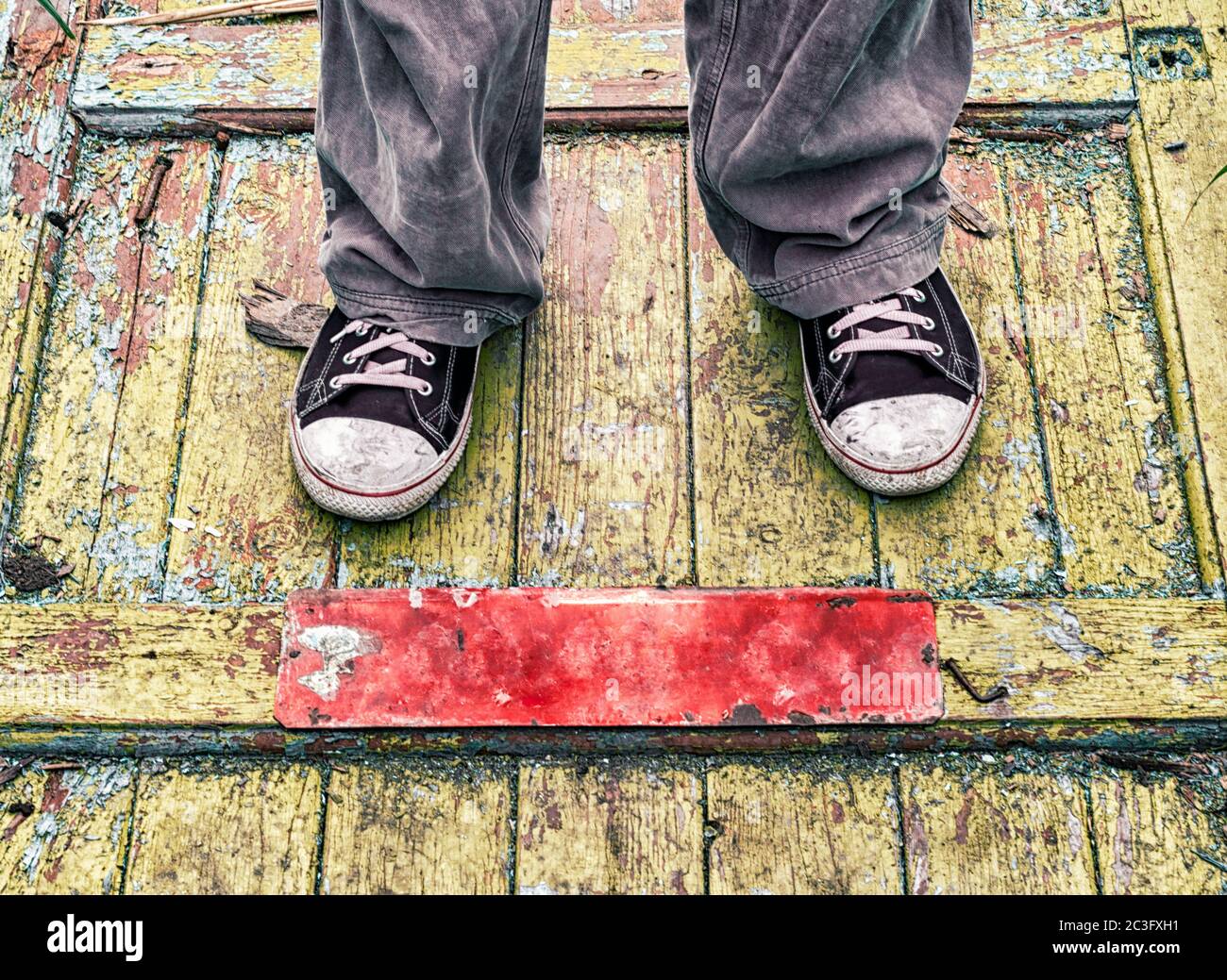 gambe di un uomo in vecchie scarpe sporche su un pavimento di legno giallo Foto Stock
