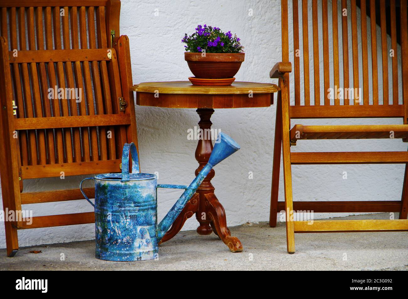 Sedie di legno ripiegate su una terrazza con un tavolo rotondo e lattina di annaffiatura blu Foto Stock