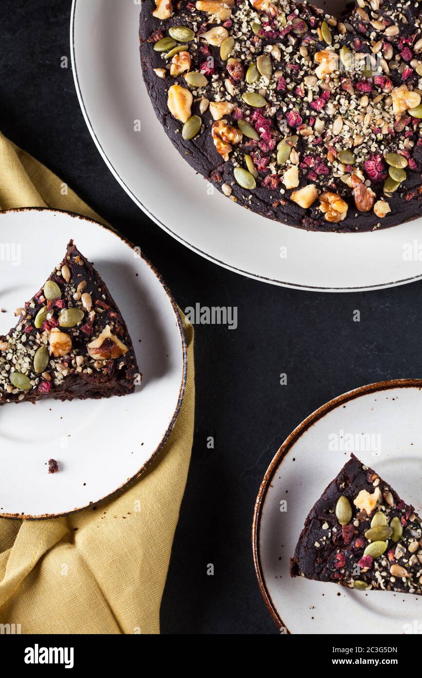 Torta al cioccolato di barbabietola e Kale e fette ricoperte di pecan, semi di zucca su un piatto bianco posto su sfondo nero Foto Stock