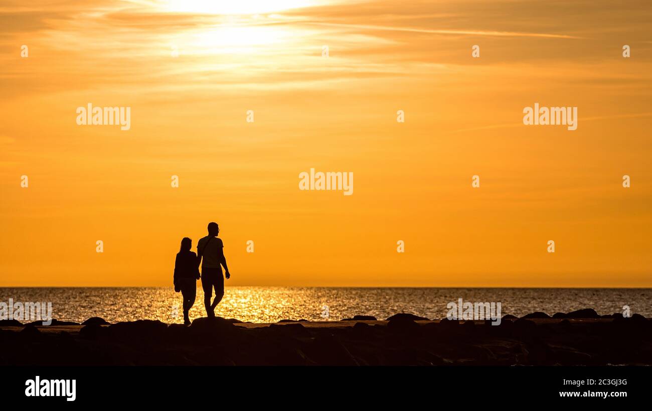 silhouette di persone a piedi e in bicicletta sul molo durante l'ora dorata del tramonto Foto Stock