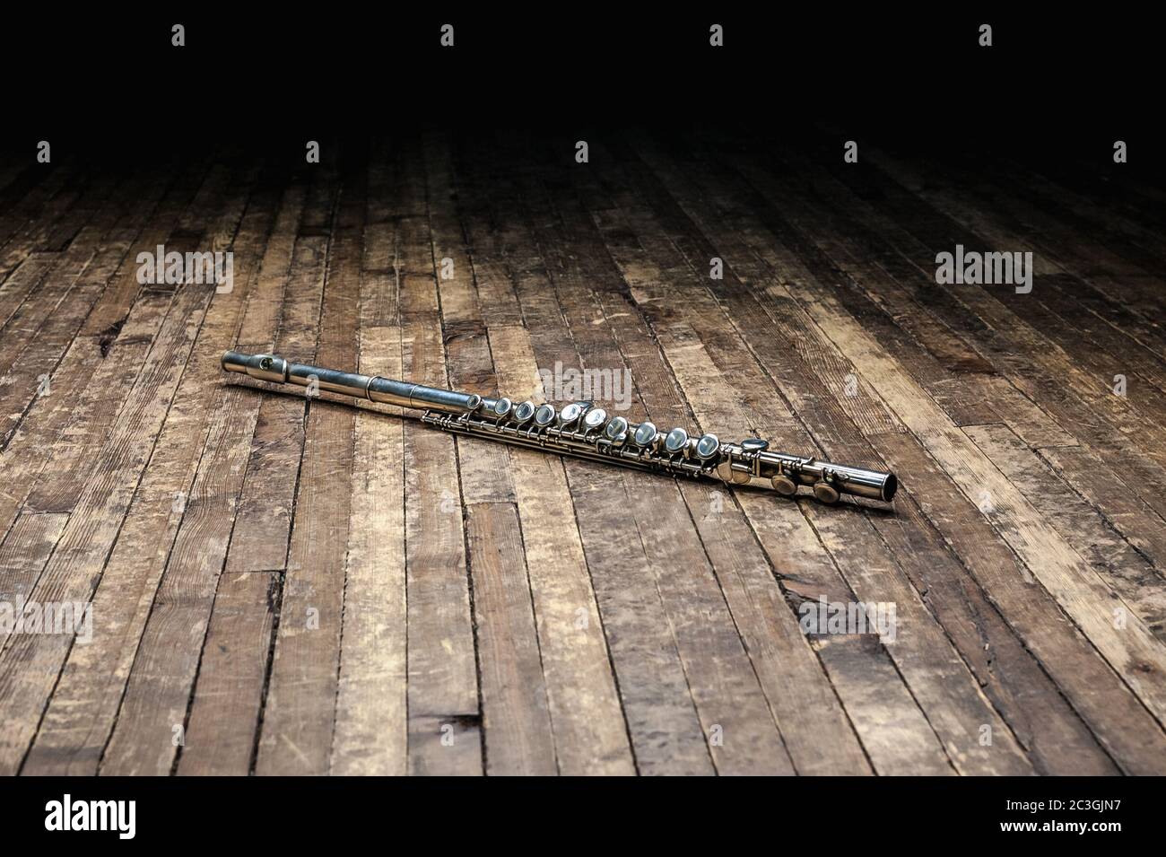 flauto di metallo argento si trova su un palcoscenico di legno al buio Foto Stock