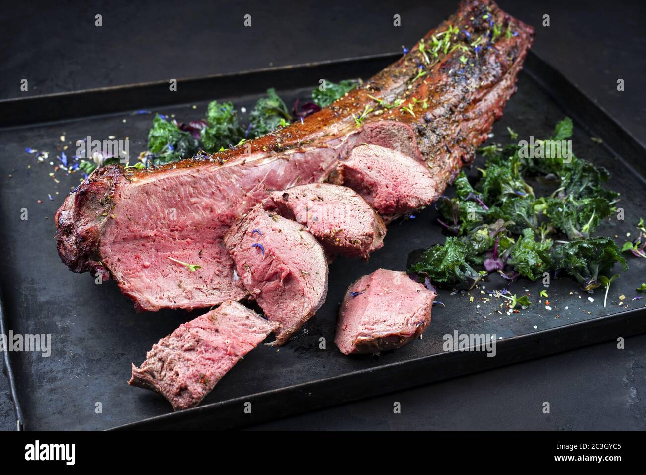 Filetto di cervo stagionato al barbecue e sella naturale con kalette offerto come closeup su una tavola rustica Foto Stock