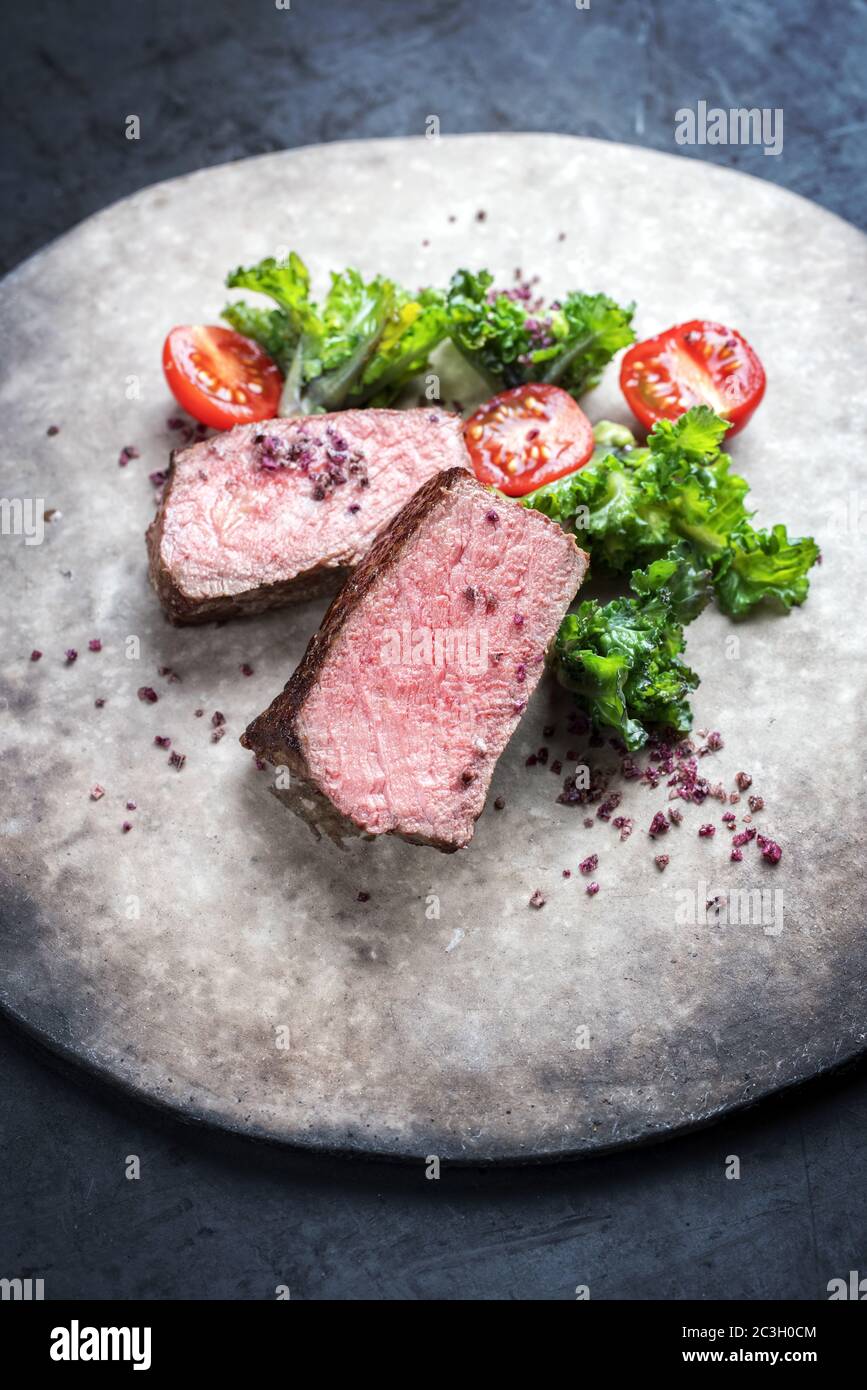 Barbecue arrosto di manzo di wagyu stagionato naturale affettato con rapini e tomatos come closeup su una piastra di design moderno Foto Stock