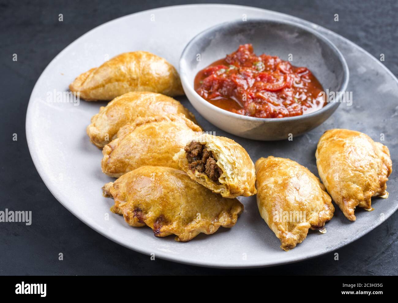 Tradizionale empanada de carne sudamericana offerto con un tuffo chili come primo piano su una piastra di design moderno Foto Stock
