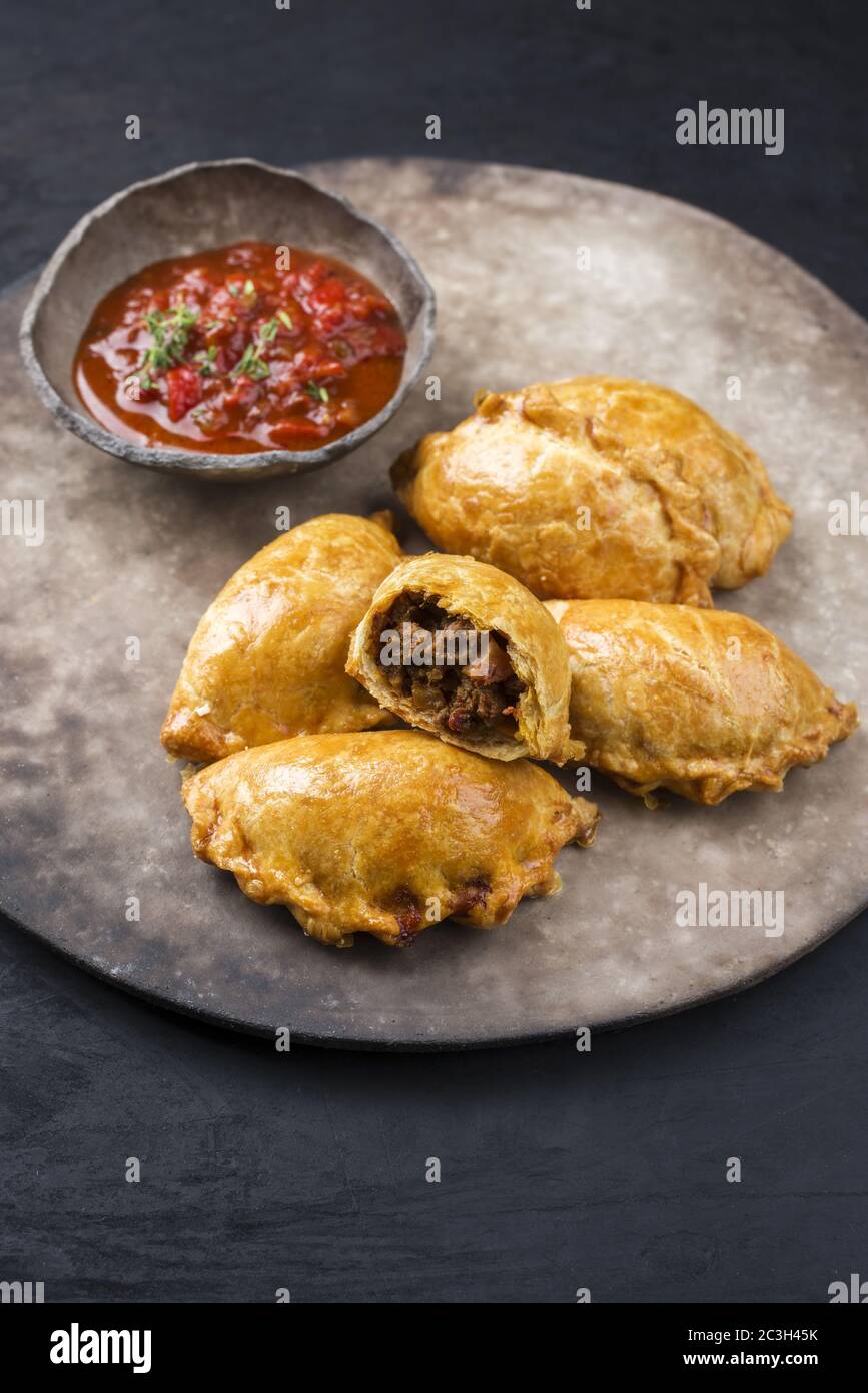 Tradizionale empanada de carne sudamericana offerto con un tuffo chili come primo piano su una piastra dal design rustico e moderno Foto Stock