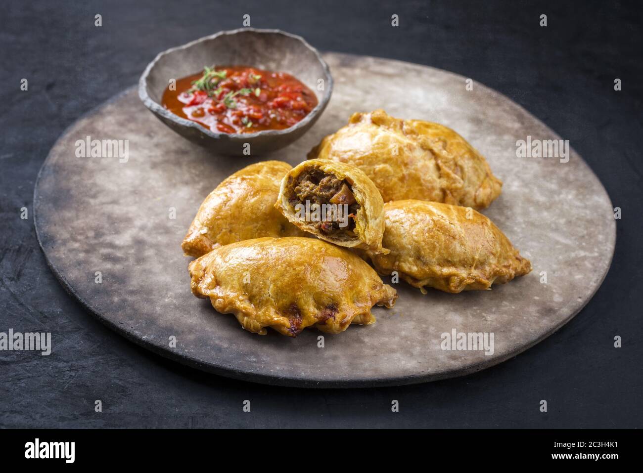 Tradizionale empanada de carne sudamericana offerto con un tuffo chili come primo piano su una piastra dal design rustico e moderno Foto Stock