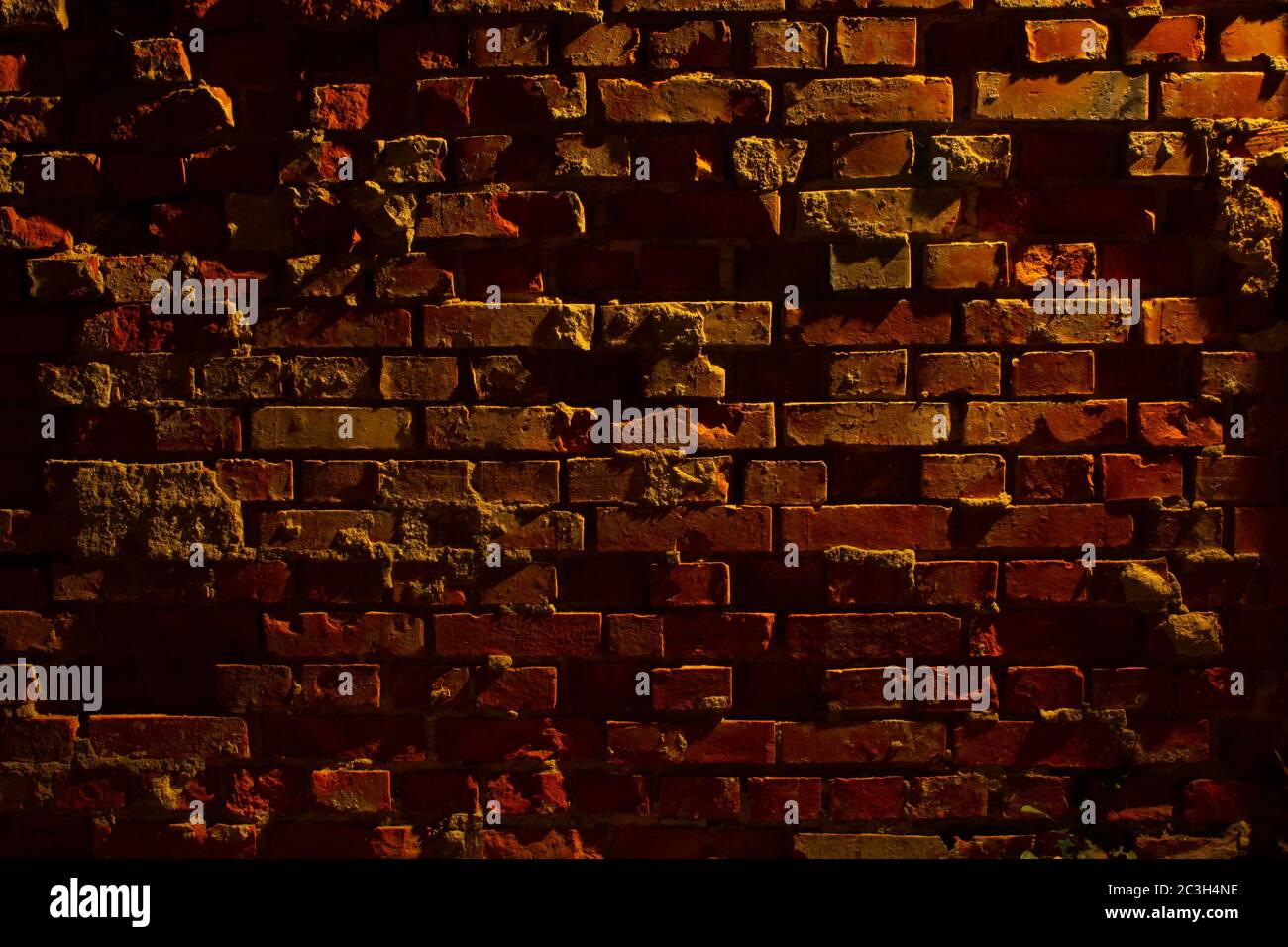 Vecchia grugia e muro di mattoni rossi danneggiato di notte con luce di una lanterna che splende su di essa Foto Stock
