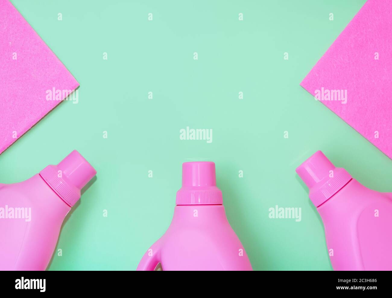 Bottiglie in plastica rosa con prodotti chimici per la pulizia, stracci per la pulizia. Delicato sfondo verde. Concetto di pulizia Foto Stock