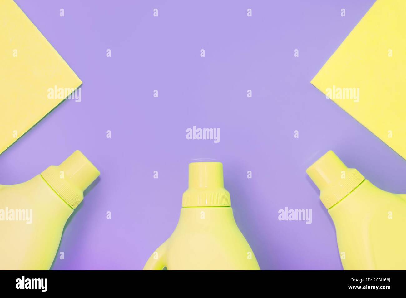 Flaconi in plastica gialli con prodotti chimici per la pulizia, stracci per la pulizia. Sfondo viola. Concetto di pulizia Foto Stock