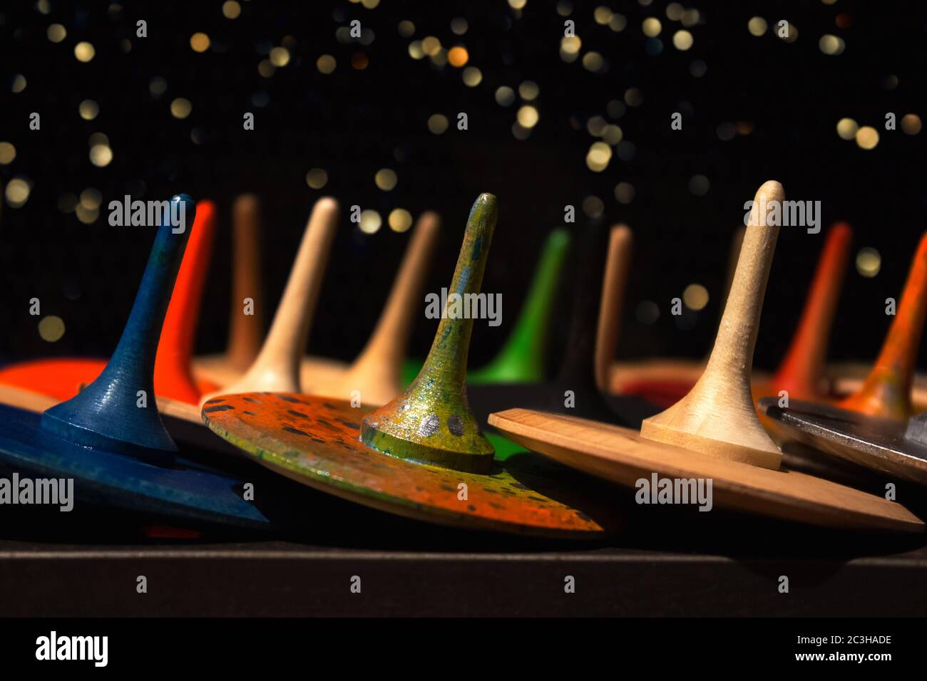 Vista frontale su colorati giocattoli in legno dipinti a mano - top con spina o whirliggs come sfondo creativo con bokeh oro chiaro sfocato Foto Stock