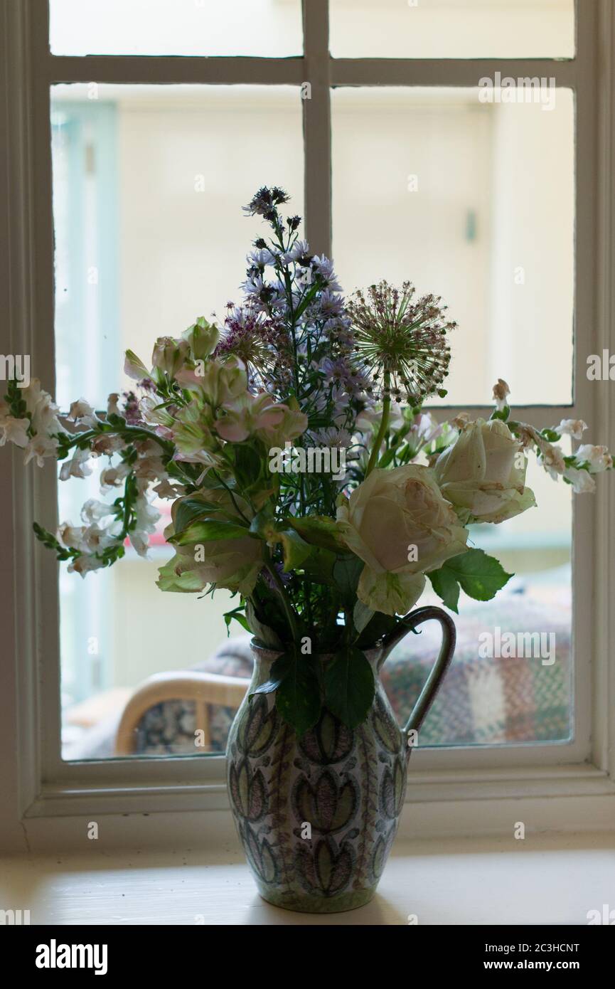 Un mazzo di fiori rosa pallido, bianchi e malva in una brocca di Denny su un davanzale Foto Stock