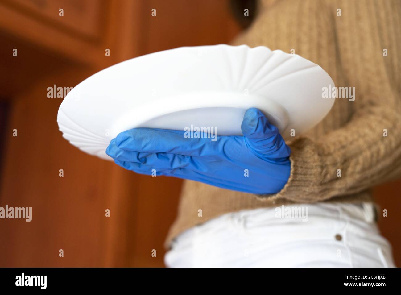 Un primo piano di una mano femminile con un guanto medico che tiene un piatto bianco Foto Stock