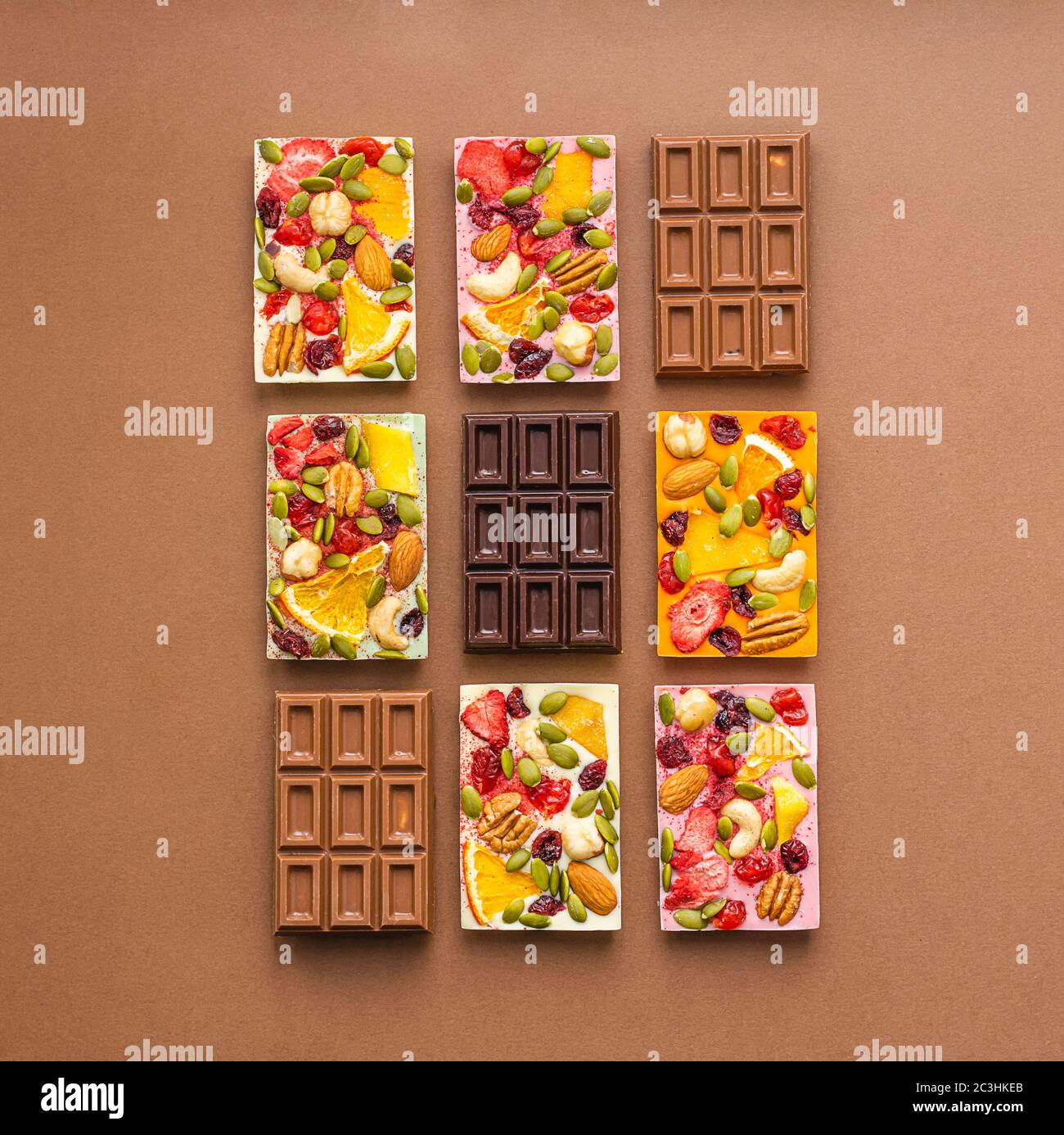 Cioccolato di vari colori e ripieni colorati con fette di frutta a guscio su fondo marrone. Layout piatto della vista dall'alto. Foto Stock