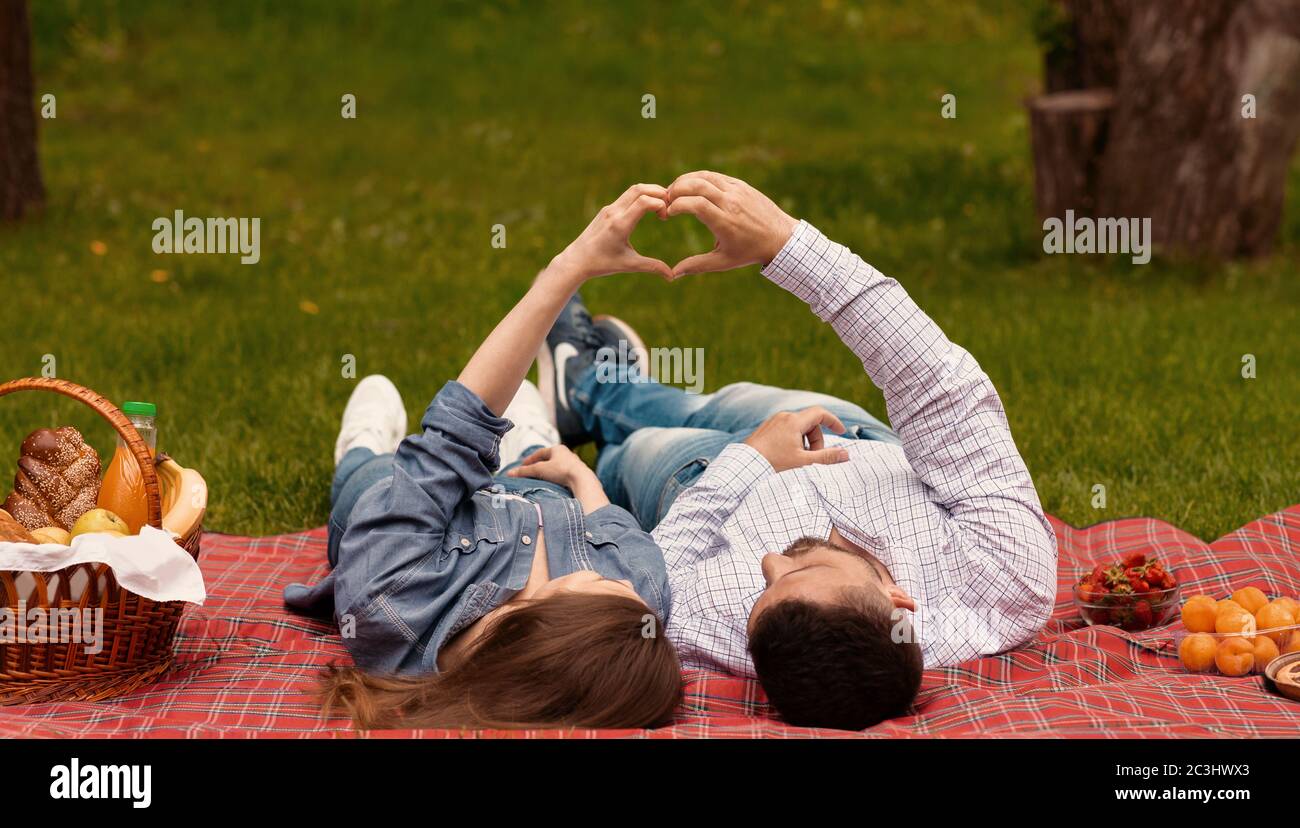 Coppia di innamorati che fanno cuore con le mani per mostrare il loro amore durante il picnic al parco Foto Stock