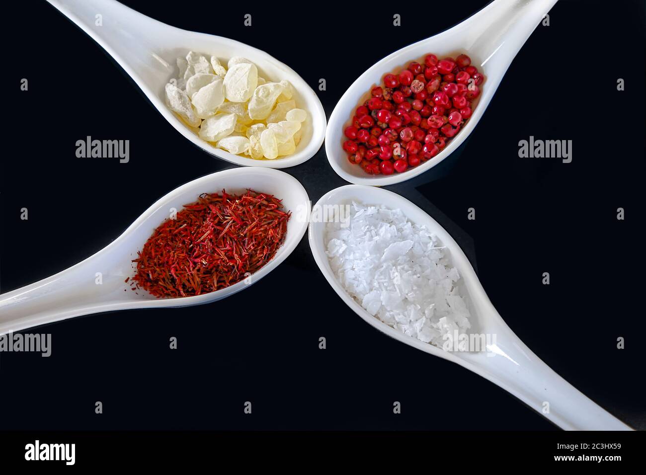 Spezie, isolate. Un assortimento di zafferano, mastika, pepe rosa e spezie in fiocchi di sale in cucchiai bianchi. Immagine stock. Foto Stock