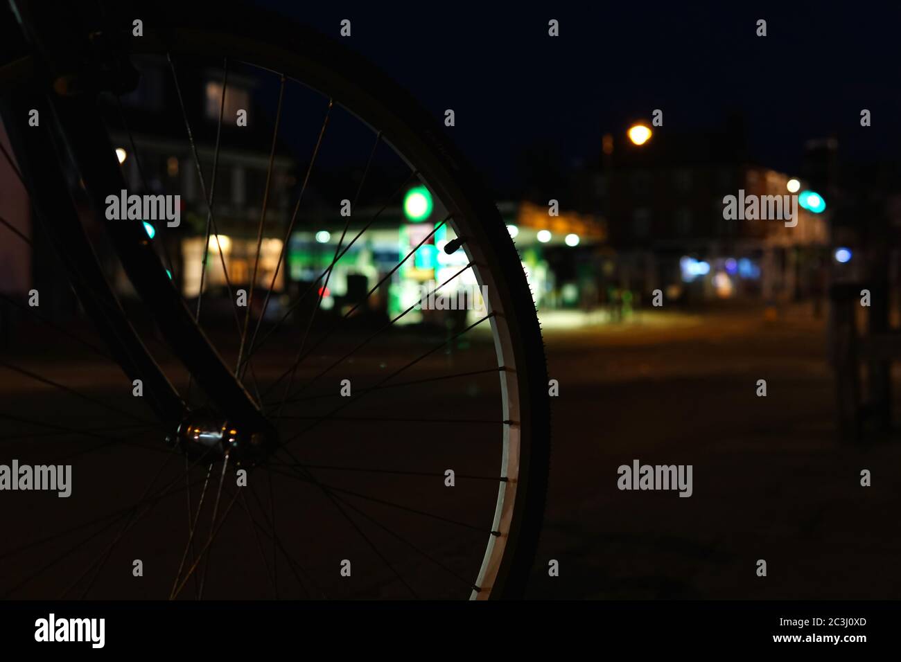 Una ruota anteriore per biciclette di notte, che mostra il cerchione della ruota e il tappo della pressione dell'aria con raggi, su uno sfondo sfocato del distributore di benzina. Foto Stock