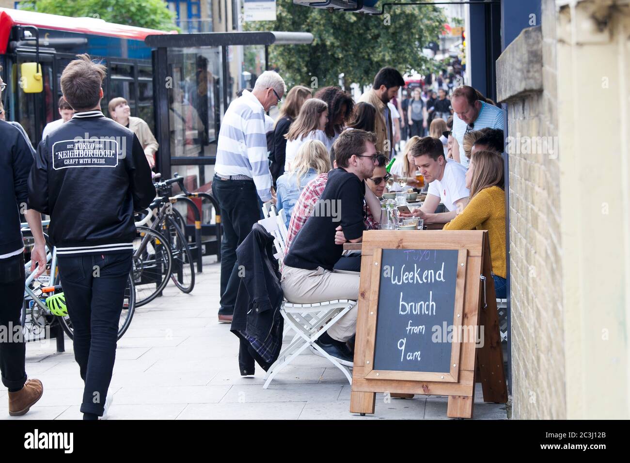 Londra, Regno Unito - 17 luglio 2019, la gente è seduta in un caffè di strada sulla trafficata Brick Lane. Un annuncio è scritto su una lavagna nera - brunch da nove Foto Stock