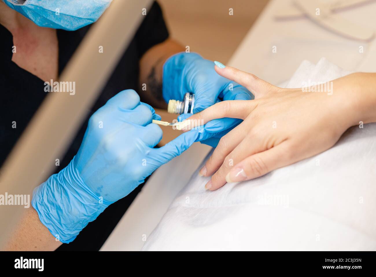 Primo piano di Beautician dipingendo i chiodi del suo cliente in vernice blu e gialla. Foto Stock