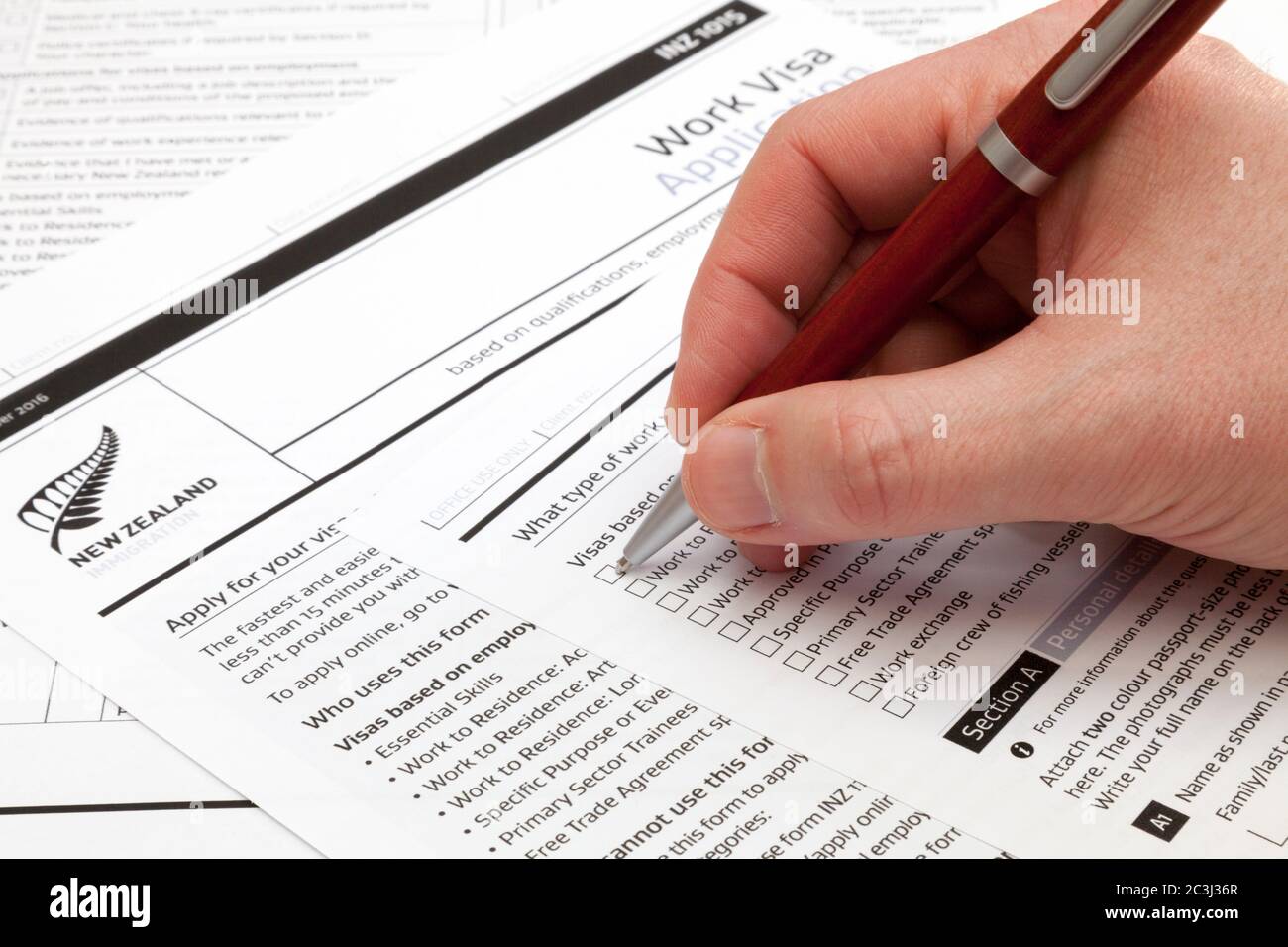 Un uomo che tiene una penna a sfera per compilare un modulo di richiesta di visto di lavoro in Nuova Zelanda. Foto Stock