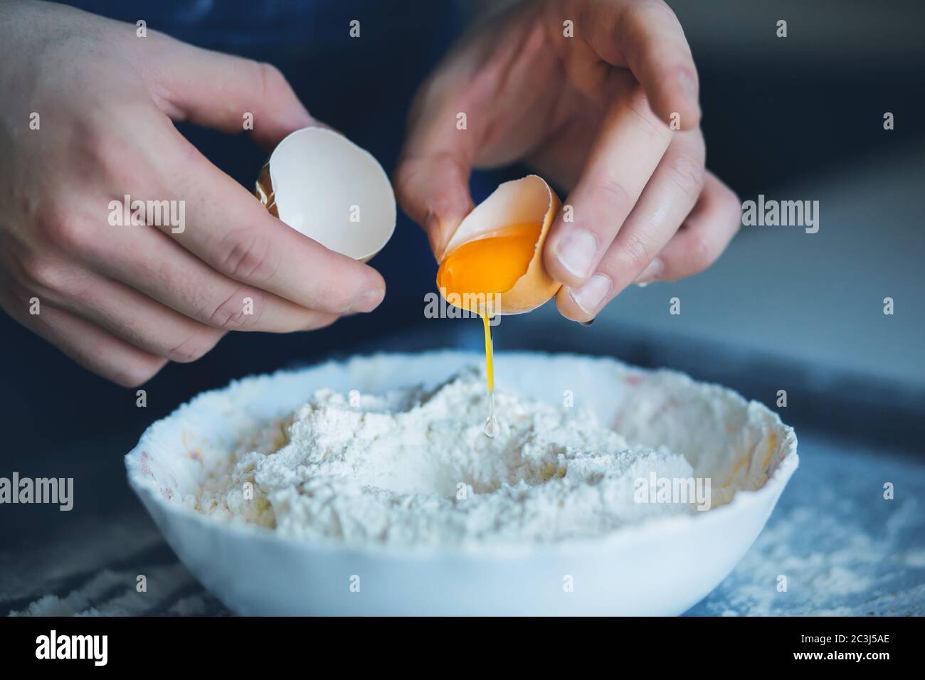 Un uomo ha rotto il guscio di un uovo di pollo e sta per versarlo in una ciotola di farina per fare l'impasto. Cucina casalinga. Foto Stock