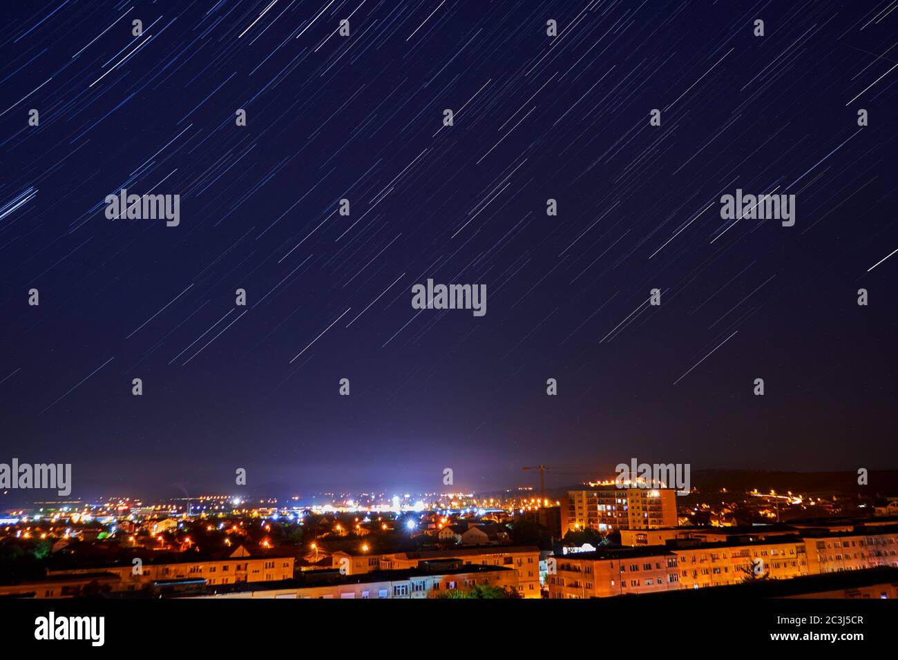 Star Trails in cielo notturno chiaro sopra la città Foto Stock