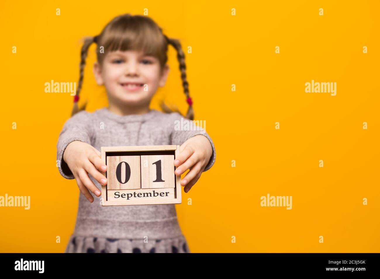 Primo piano ritratto di prima ragazza grader con spirali divertenti guardando la fotocamera e tenere in legno calendario fissato il 1 settembre isolato su luminoso YE Foto Stock