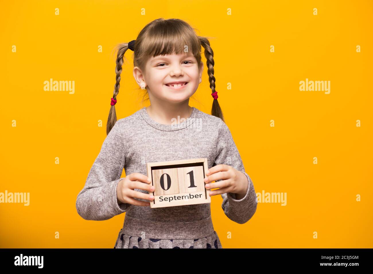 Primo piano ritratto di prima ragazza grader con spirali divertenti guardando la fotocamera e tenere in legno calendario fissato il 1 settembre isolato su luminoso YE Foto Stock