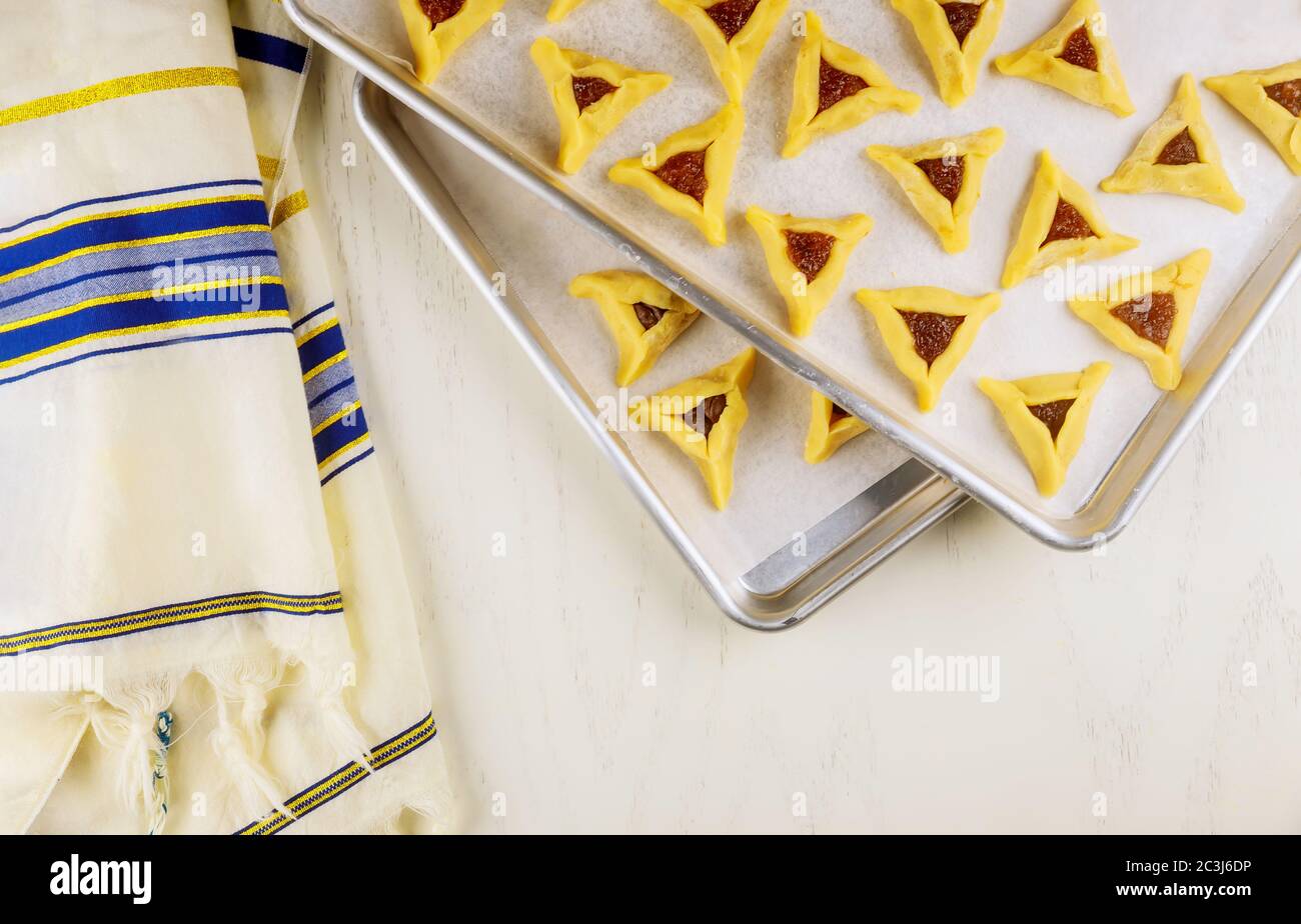 Biscotti ebrei di hamantaschen crudi su vassoio da forno con tallit per Purim. Foto Stock