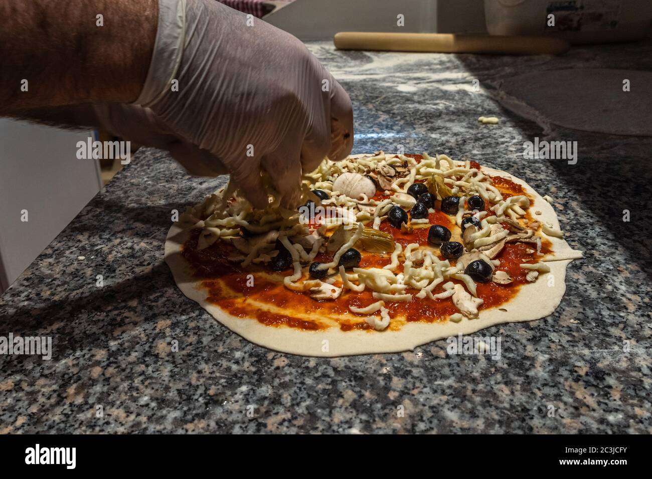 Preparazione della pizza italiana. Pizza Four Seasons. Salsa, funghi, olive nere, carciofi, mozzarella Foto Stock