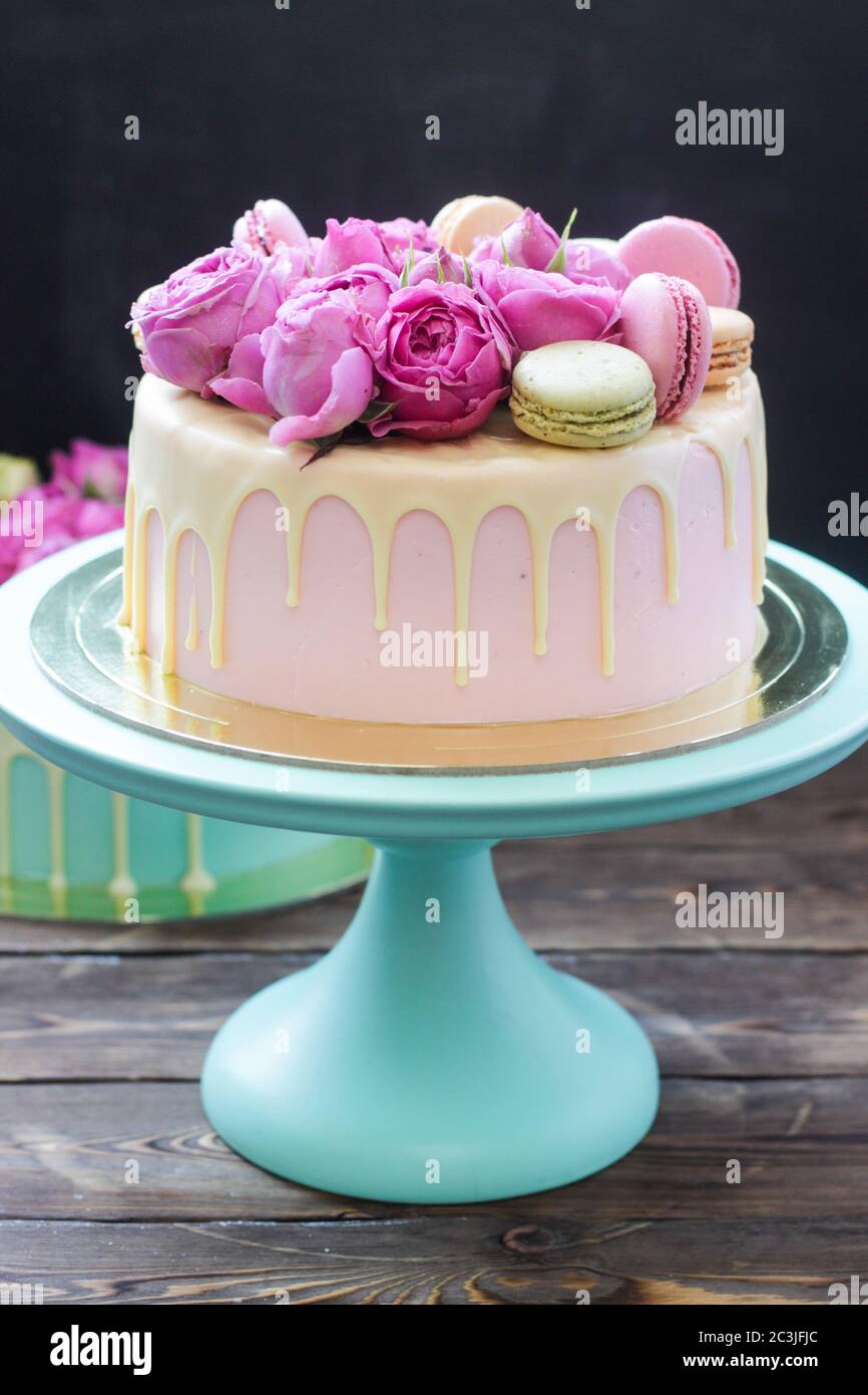 Elegante torta di nozze rosa decorata con cioccolato bianco fuso, belle rose  fresche e macaron francesi. Sfondo nero Foto stock - Alamy