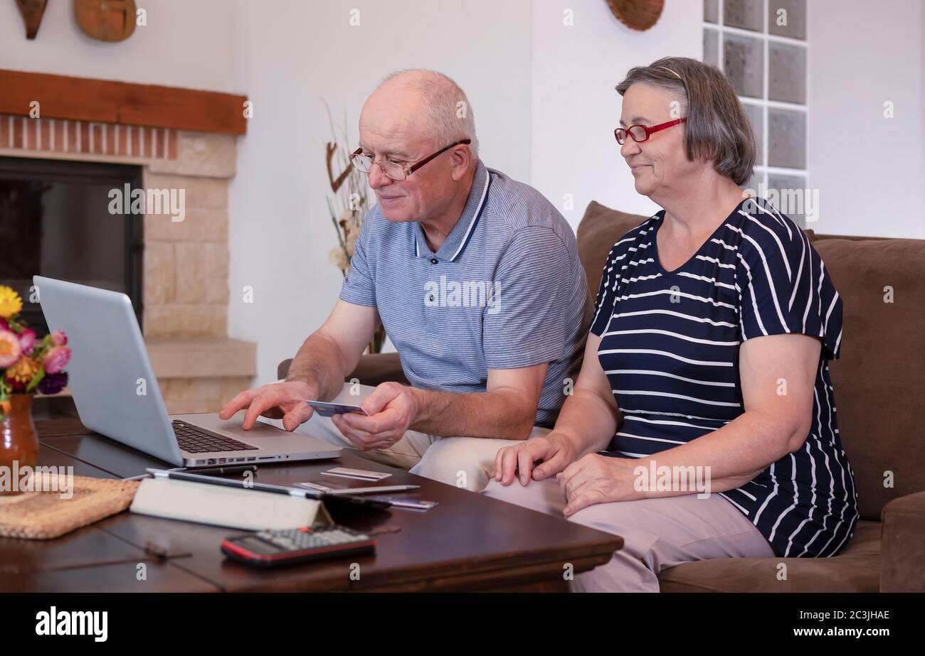 Coppia senior che acquista online su un computer portatile utilizzando la carta di credito a casa. Internet banking a casa. Focus sul volto dell'uomo anziano Foto Stock