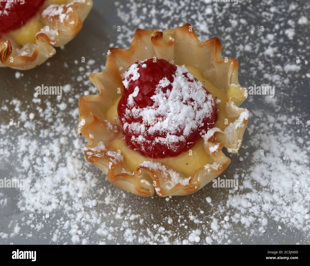 Crostata di lamponi con crema e zucchero in polvere in una tazza di pasticceria Foto Stock