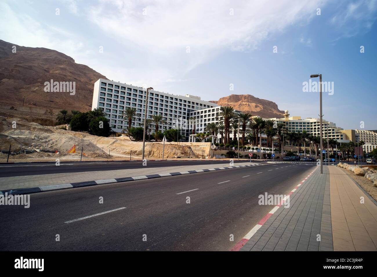 Strada asfaltata in primo piano. Strade di una piccola città mediterranea con palme e cime di montagna in mezzo al deserto. Piccola città di Ein Foto Stock