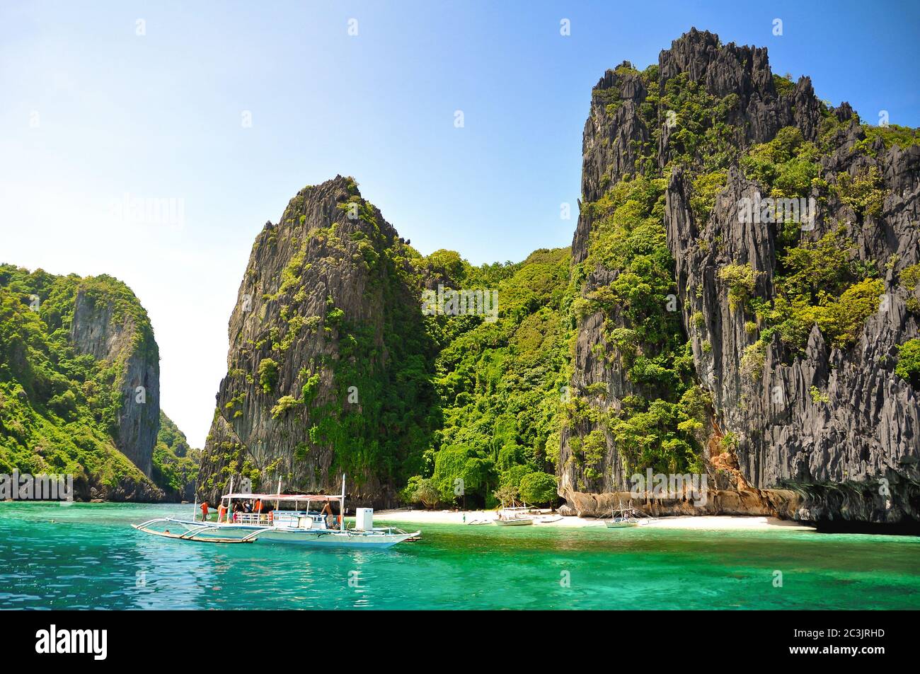 Splendido paesaggio tropicale con acque turchesi e scogliere verdi, barca turistica in oceano, El Nido, Palawan, Filippine Foto Stock