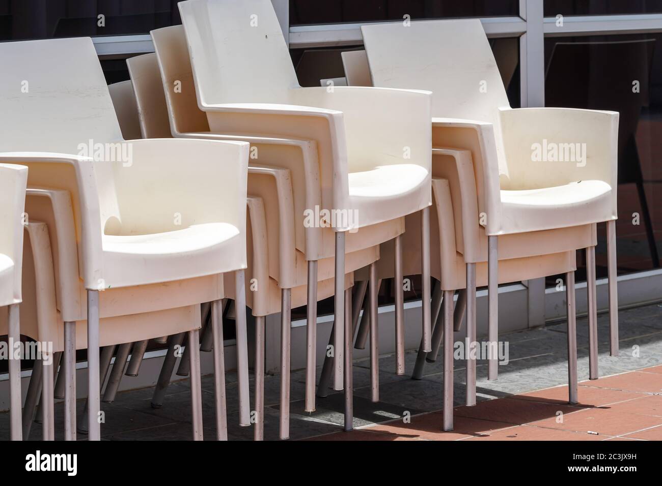 sedie di plastica bianca moderne e contemporanee accatastate contro finestre di vetro Foto Stock