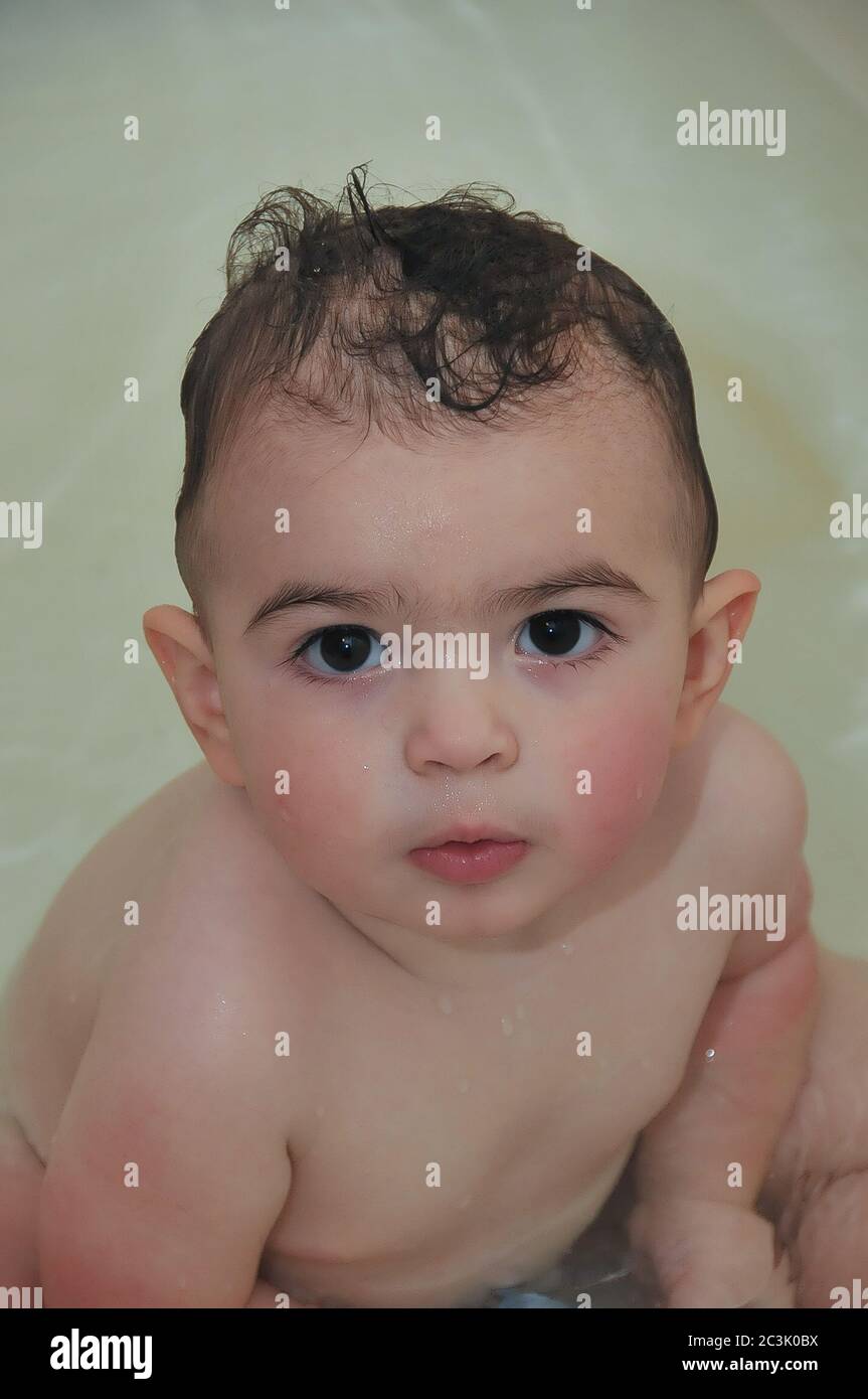 Un bambino carino con un'espressione seria guarda direttamente nella macchina fotografica mentre è dato un bagno. Foto Stock