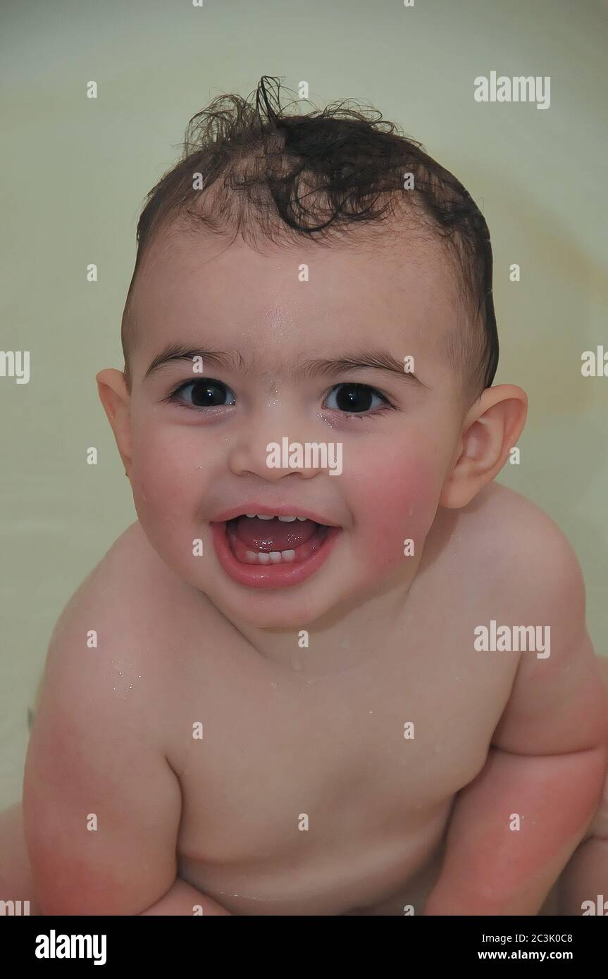 Un bambino sorridente carino nella vasca da bagno guardando direttamente nella macchina fotografica e ridendo. Foto Stock