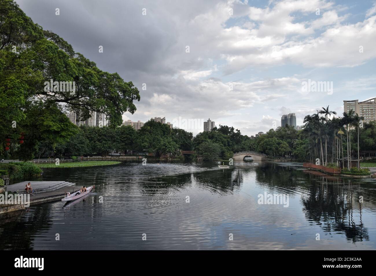 Parco cinese con il lago all'interno, acqua riflesso sulla superficie, edificio moderno in piedi sullo sfondo. Foto Stock