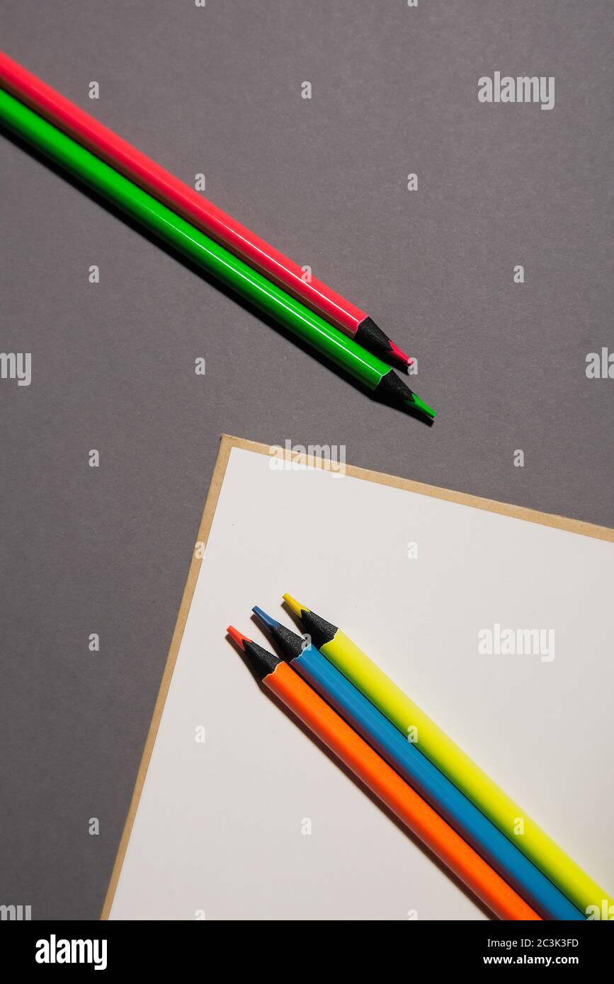notebook da scuola bianca e matite colorate su sfondo grigio, vista dall'alto Foto Stock