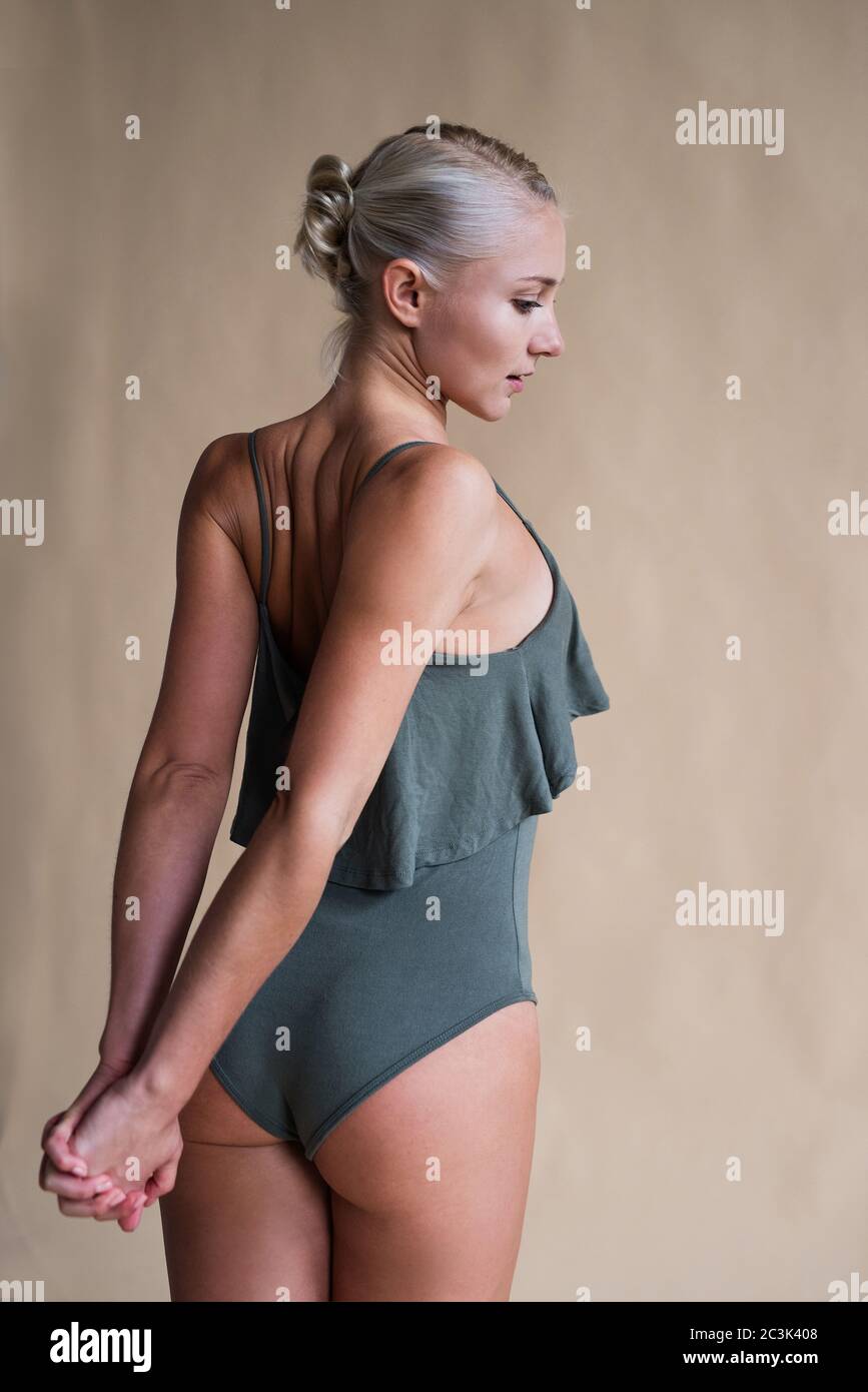 la ragazza giovane con la pelle abbronzata e i capelli bianchi sta in piedi in costume da bagno, tira indietro le mani Foto Stock