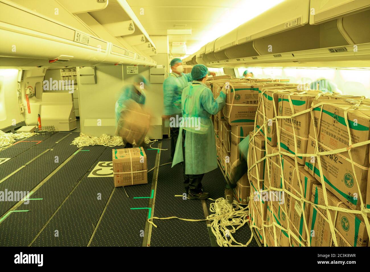 Caricatori cinesi che indossano abiti da muta caricando un passeggero convertito in aereo da freighter con maschere chirurgiche e camici per combattere il Pandemia COVID Foto Stock